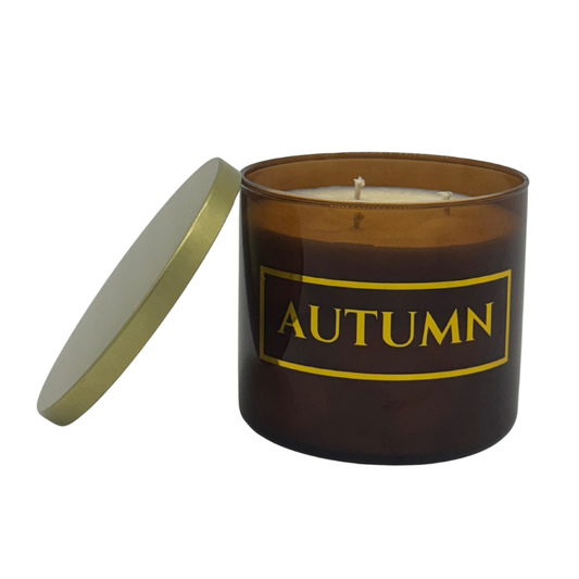 Candle in an amber container with 'AUTUMN' text in gold on a white background