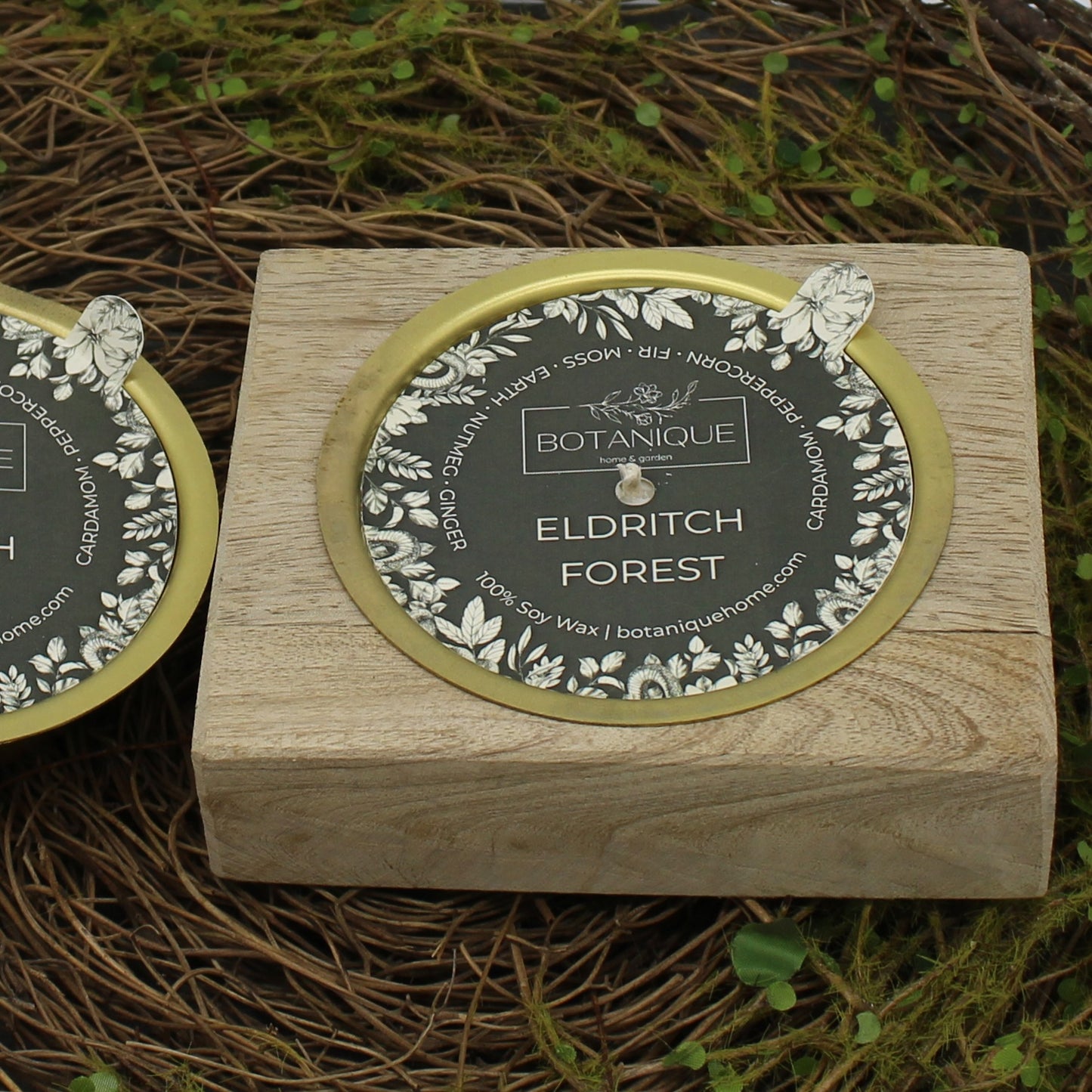Wooden candle holder with 'Botanique Eldritch Forest' candle label on a natural mossy background