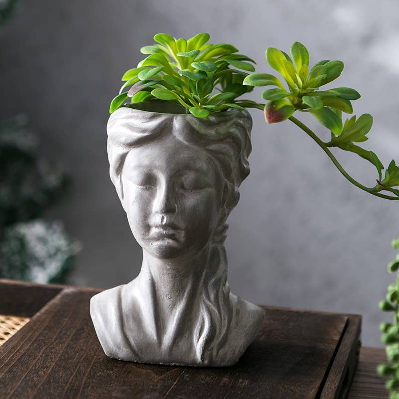 Bust sculpture with a plant growing out of it on a wooden surface.
