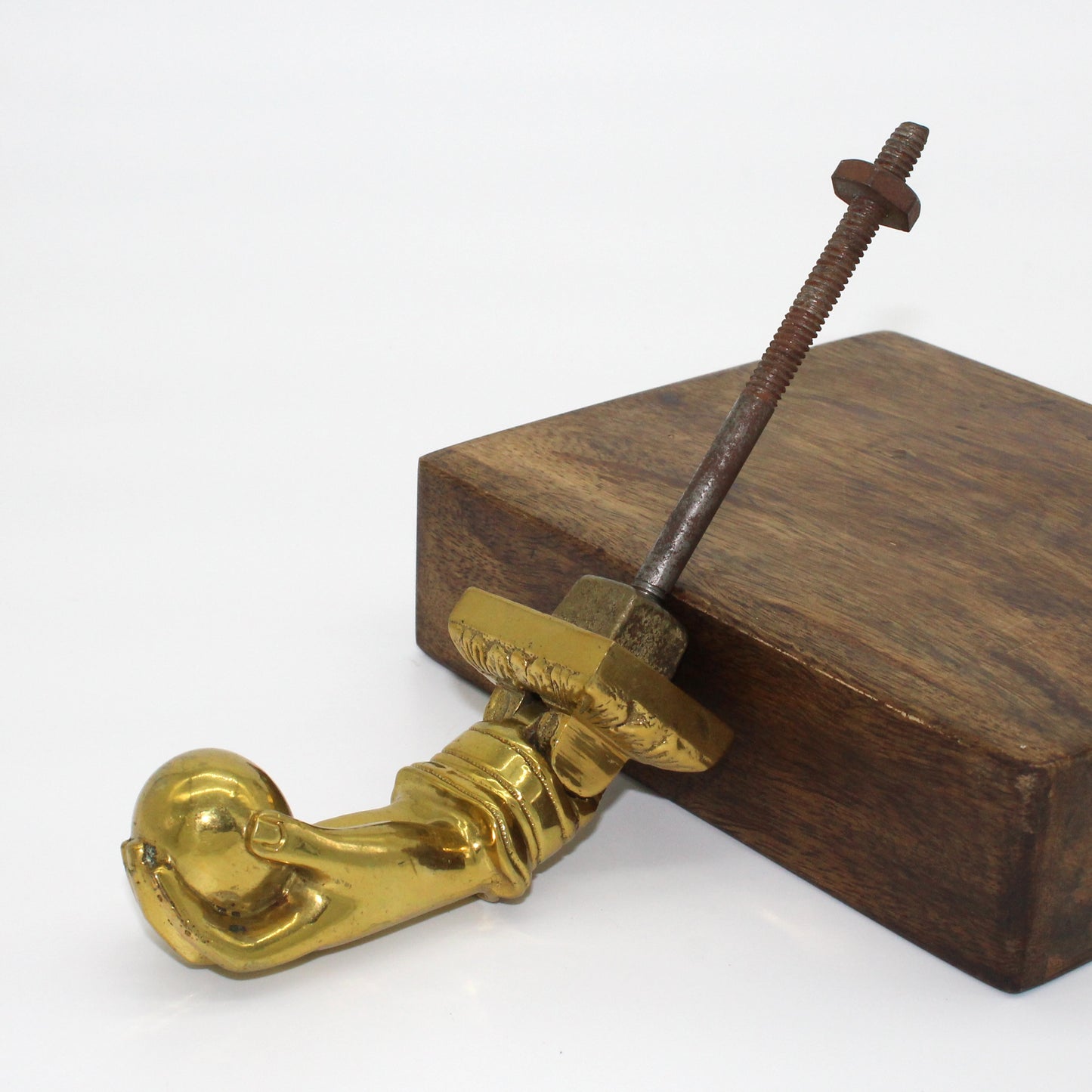 Gold door handle propped against a wooden block with a long screw on a white background