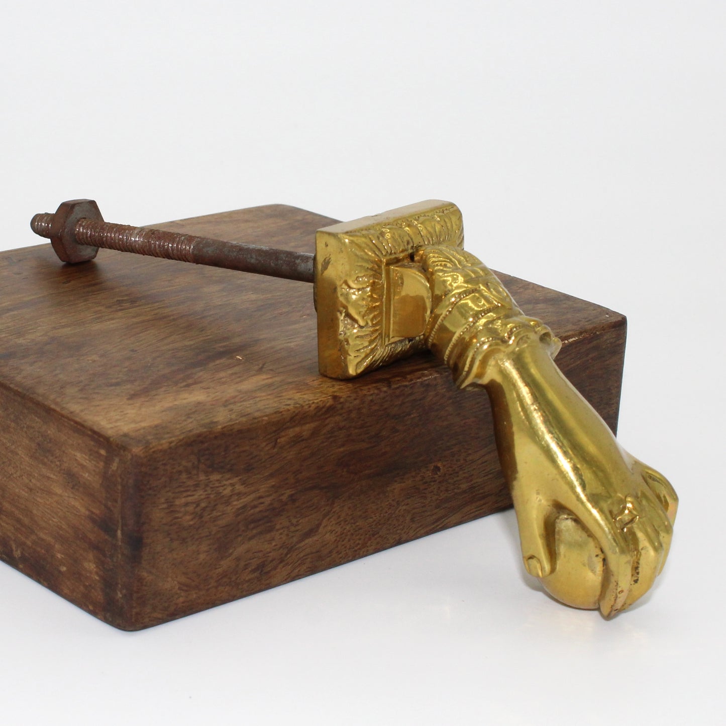 Brass hand door knocker sits on wood with a view of the ring and sphere the hand is holding.