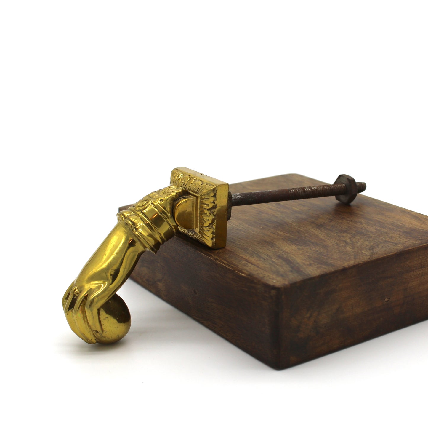 Decorative polished brass door knocker shaped like a hand holding a sphere sits on wood with a white background.