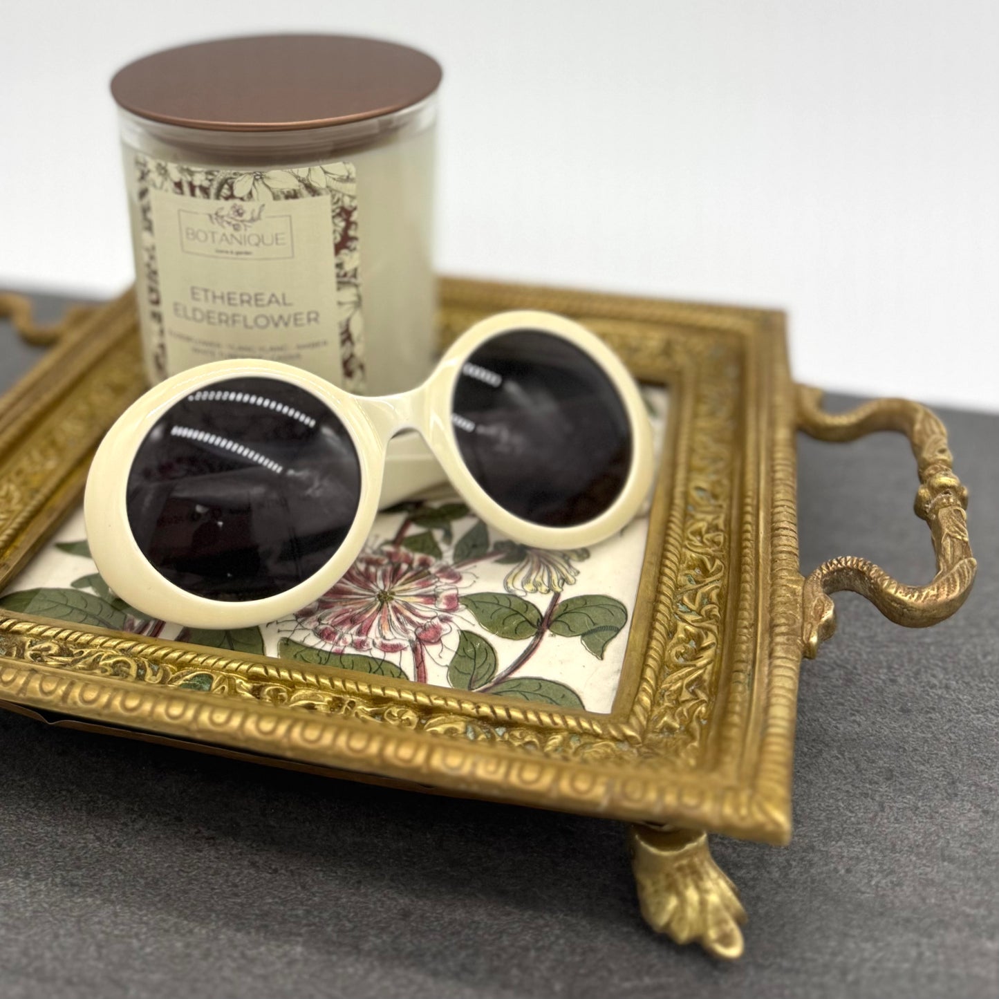 Round sunglasses with black lenses on a decorative tray with a candle in the background