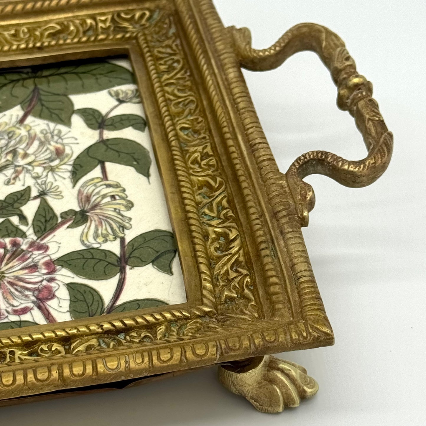Decorative brass tray closeup with floral tile insert on a white background.