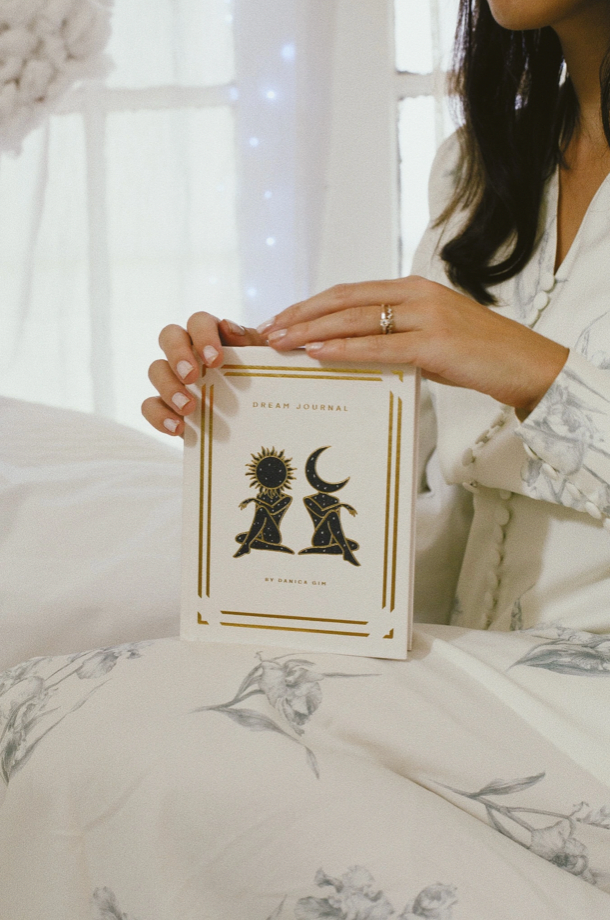 Person holding a book titled 'Green Journal' with celestial designs on a soft, light-colored surface.
