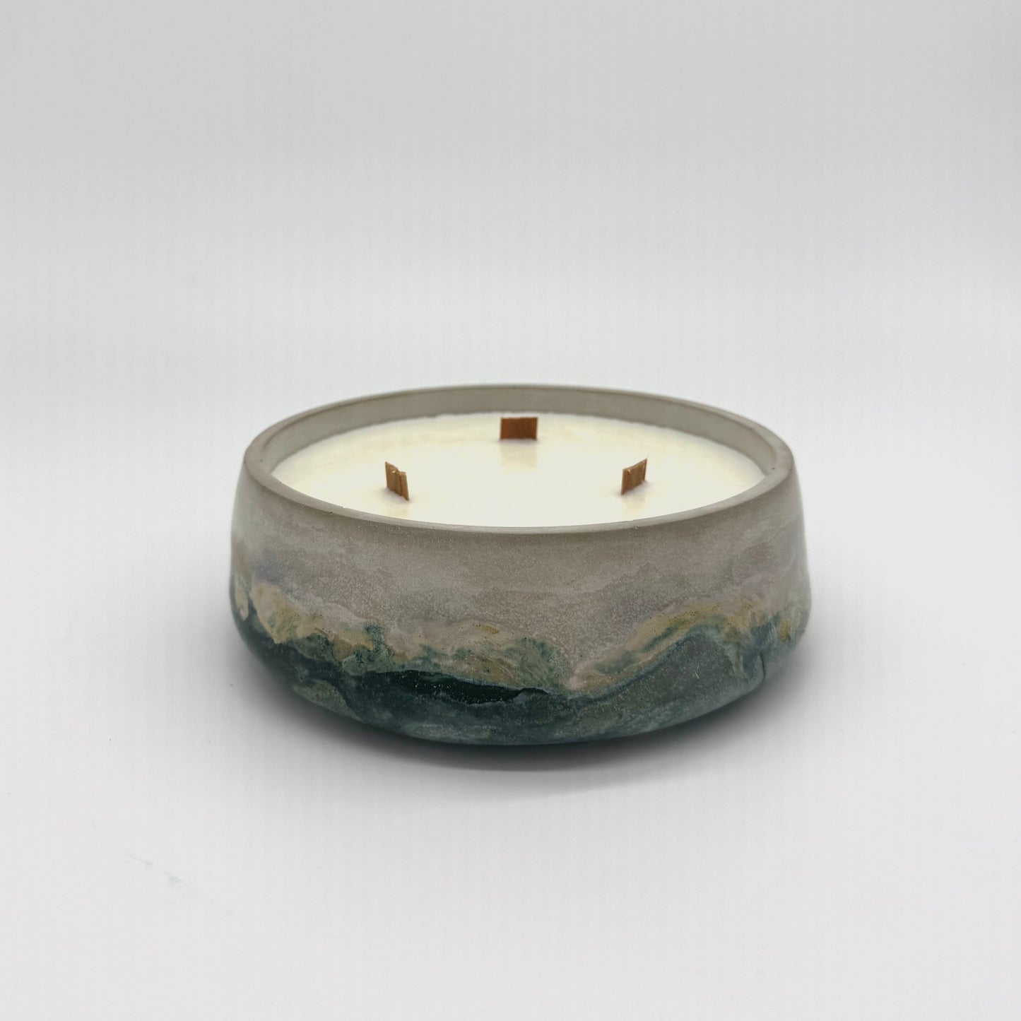 Concrete candle with three wicks in a gray bowl swirled with dark green and gold on a white background
