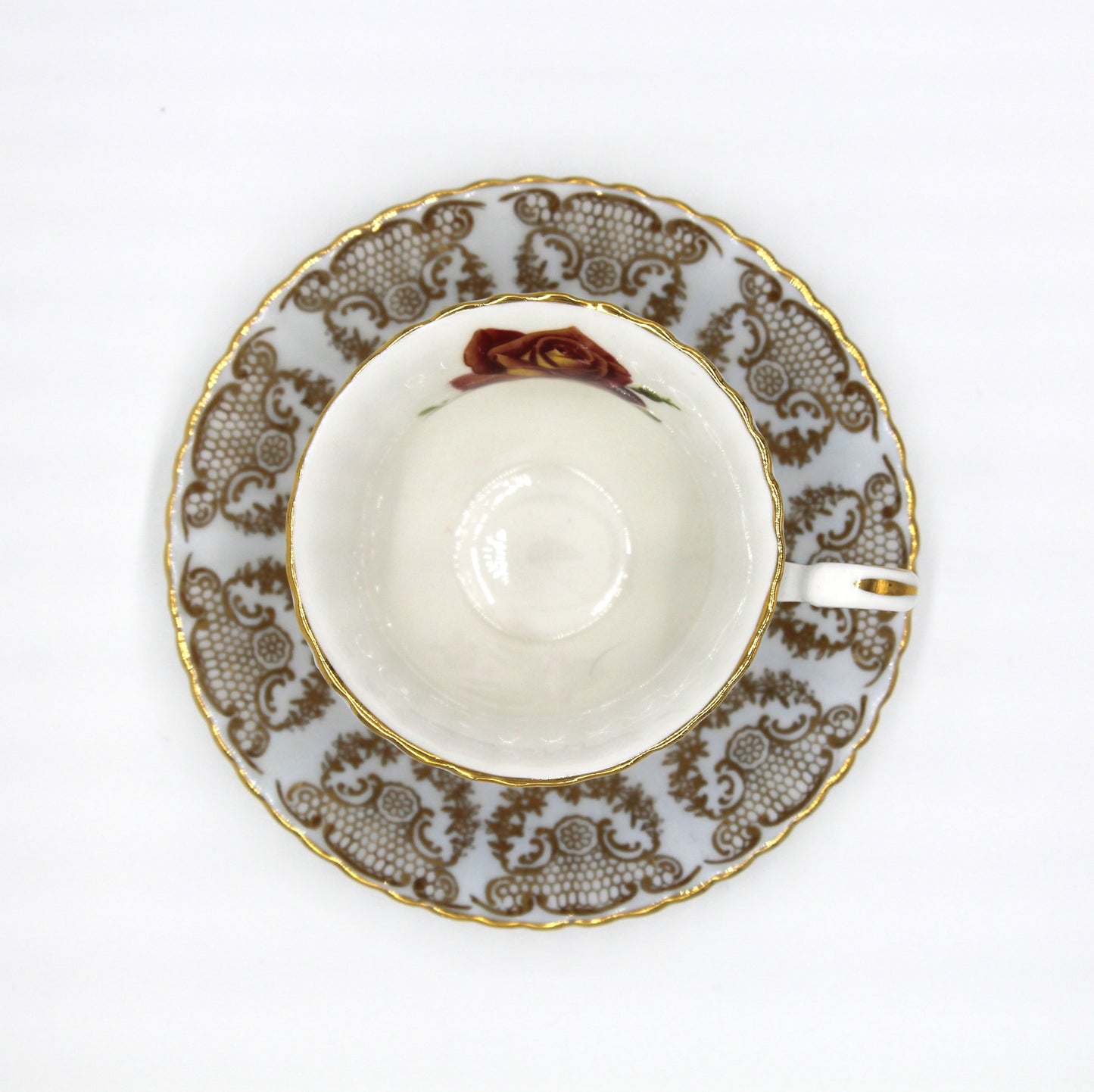 White teacup and saucer with gold and brown floral patterns on a white background