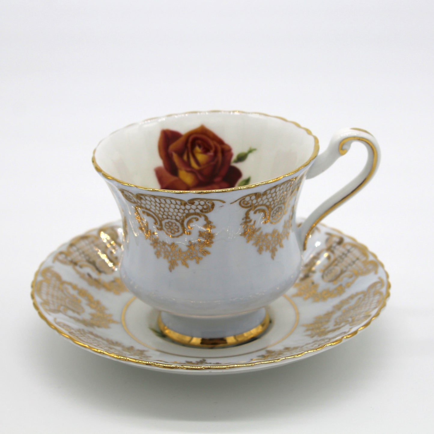 White teacup with gold detailing and a red rose on a matching saucer against a white background