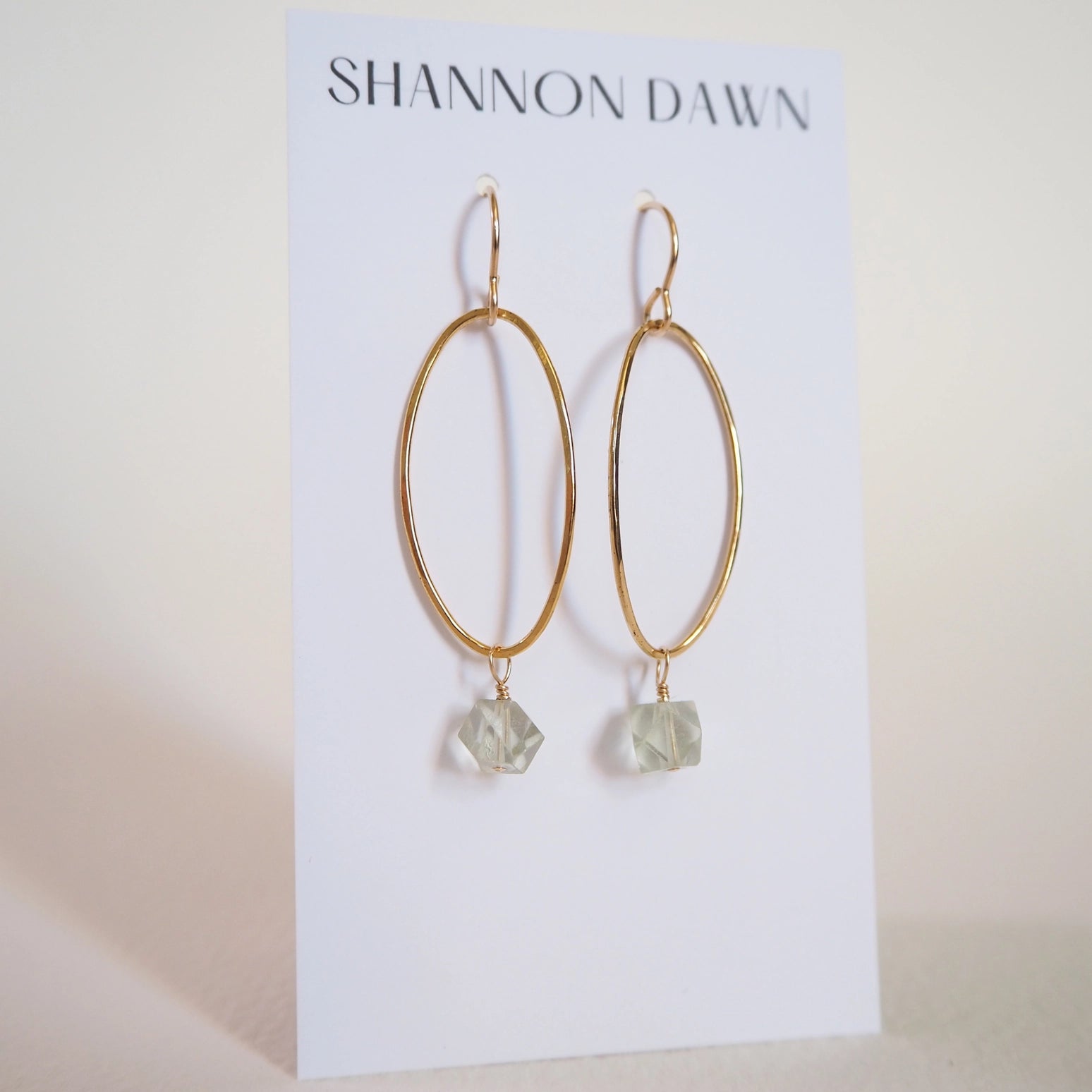 Gold hoop earrings with faceted light aqua green stones on a Shannon Dawn card.