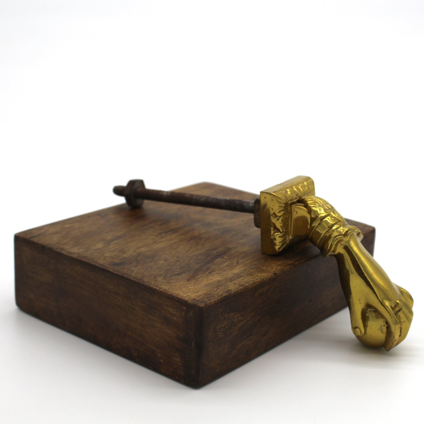 A polished brass door knocker shaped like a hand holding a sphere sits on a piece of wood with a white background.