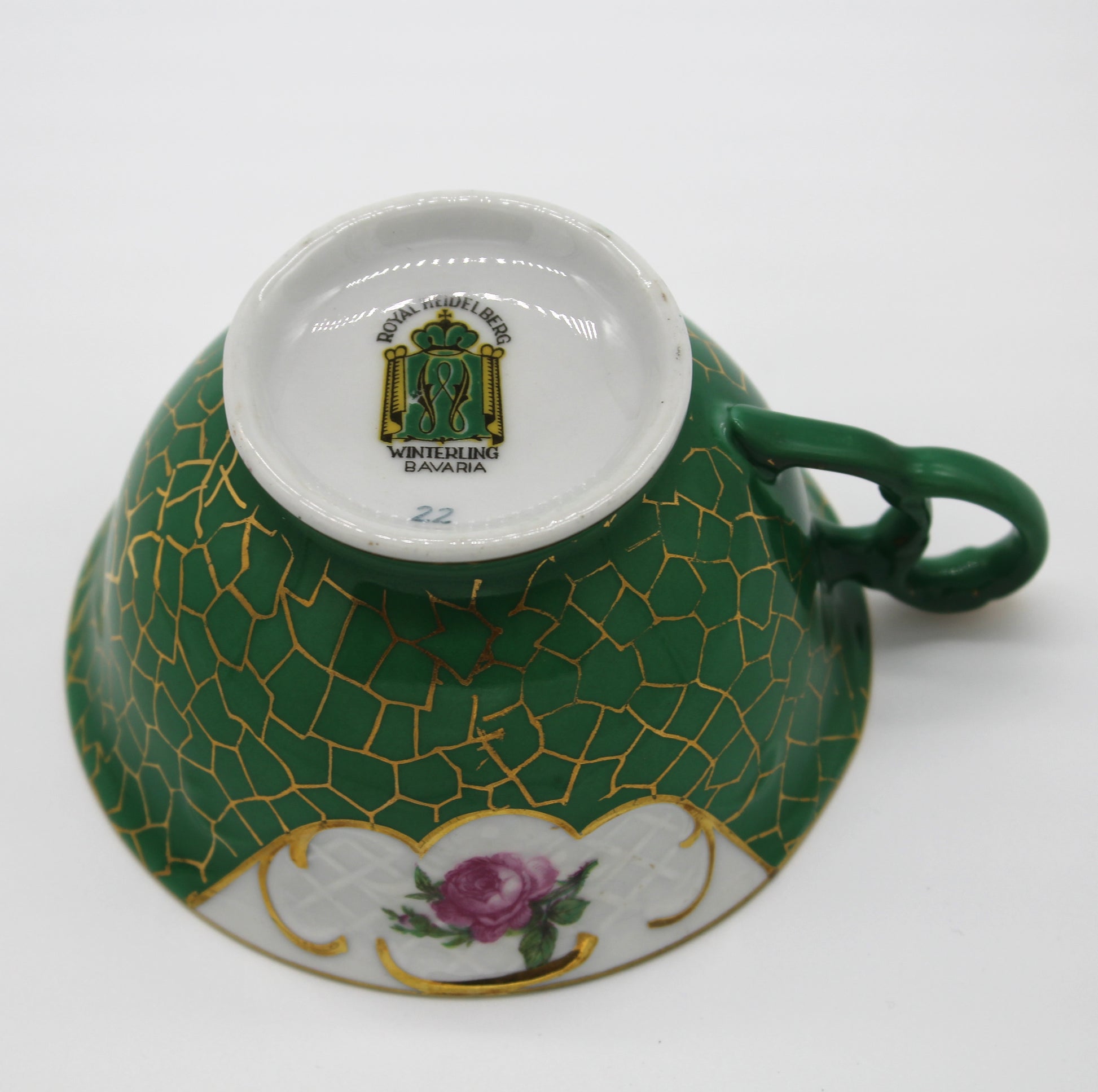 Green teacup with gold patterns and a floral design on a white background