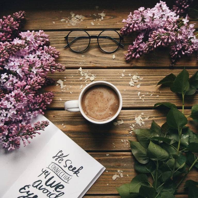 Cup of coffee with flowers and glasses on a wooden surface