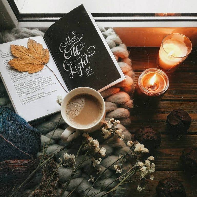 Book with a leaf, cup of coffee, and candles on a wooden surface
