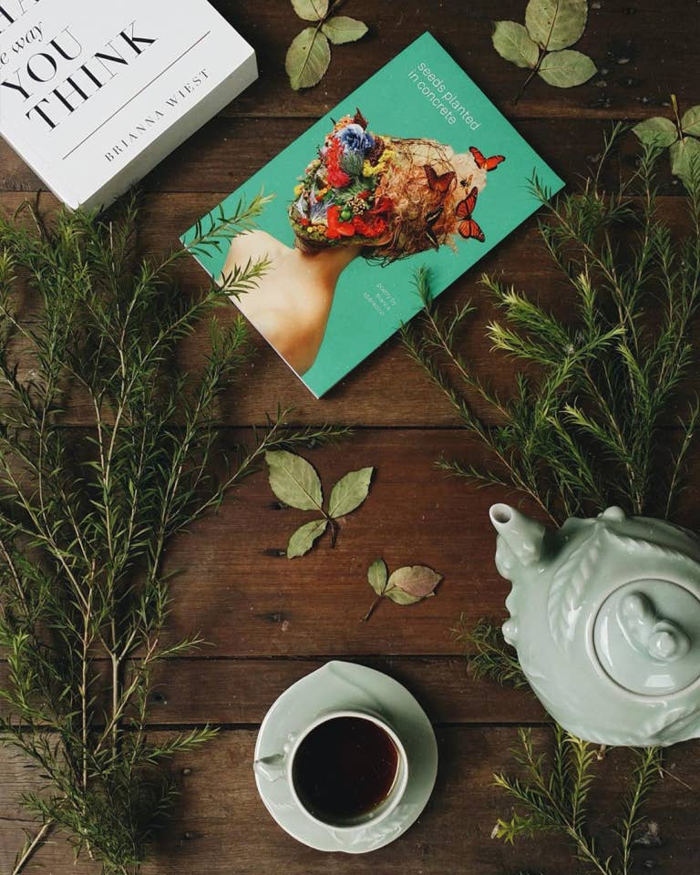 Tea cup, teapot, and book on a wooden surface with greenery