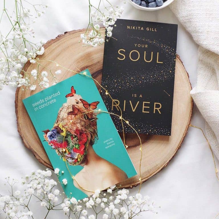 Two books on a wooden surface with flowers and a bowl of blueberries.