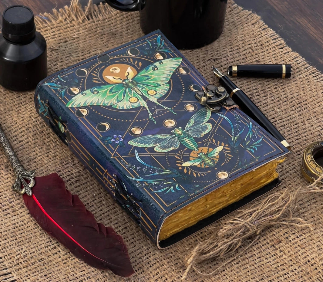 Decorative notebook with luna moth and flying insect design on a textured surface with ink bottle and feather.